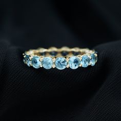 a gold ring with blue topaz stones on black fabric background, close up view