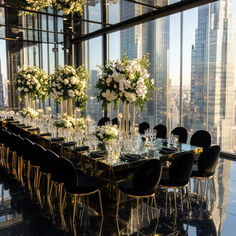 a long table is set up with black chairs and vases filled with white flowers