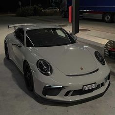 a white sports car parked in front of a gas station sign at night with the lights on