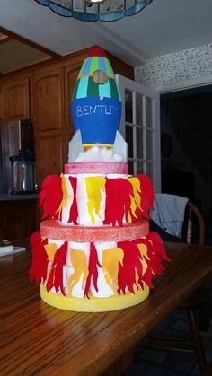 a multi - tiered cake is decorated with red, yellow and blue paper cutouts