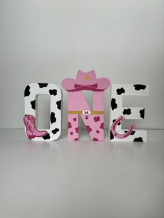 the word one is decorated with pink and black polka dots, cowboy boots, and a cow print