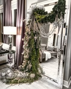 a mirror decorated with christmas greenery and beads in a living room area, next to a table lamp