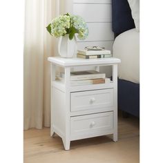 a white nightstand with two drawers and a vase filled with flowers on top of it