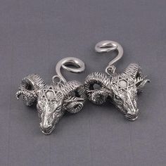 pair of silver oxen earrings with ram heads on them, sitting on a gray surface