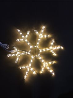 a snowflake made out of small lights on a black background with the cord plugged in