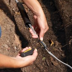 two hands holding scissors in the dirt with wires attached to them and another person's hand