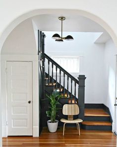 a chair sitting in front of a stair case next to a potted plant on top of a hard wood floor