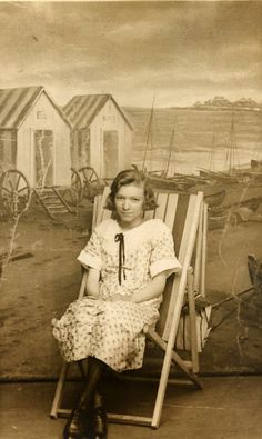 an old black and white photo of a woman sitting in a chair on the beach