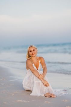 a woman is sitting on the beach and posing for a photo in front of the ocean