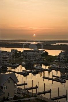 the sun is setting over a marina with boats and houses in the water near by