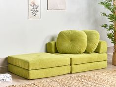 a green couch sitting on top of a wooden floor next to a potted plant