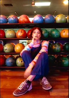 a woman sitting on the floor in front of bowling balls