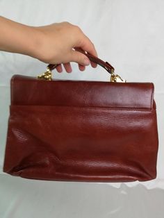 "Vtg leather cognac brown/reddish brown handbag with handle. Golden tone closure. Briefcase bag. Women`s retro purse. Inside brown vegan leather lining, 3 large compartments and 1 zip compartment. materials: leather shell; vegan leather lining condition: great vintage. The closure works well. Without serious damages. Some streaks on the leather surface (maybe 3 small). measurements: bottom width 32,5 cm / 12.7\" in height without handle 22,5 cm / 8.8\" in thickness 12 cm / 4.7\" in handle drop 1 Brown Briefcase With Handles For Business, Brown Office Briefcase With Handles, Brown Office Briefcase, Brown Double Handle Satchel For Formal Use, Brown Business Satchel With Handles, Formal Cognac Satchel With Handles, Retro Burgundy Rectangular Bag, Retro Leather Box Bag With Top Handle, Retro Leather Top Handle Box Bag