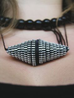 a woman wearing a black and white beaded necklace with an unusual design on it