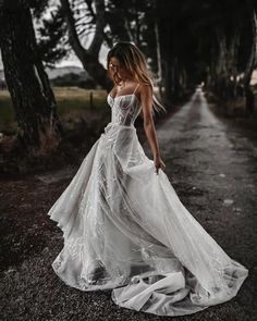 a woman in a white dress is standing on the road with trees behind her and looking at the camera