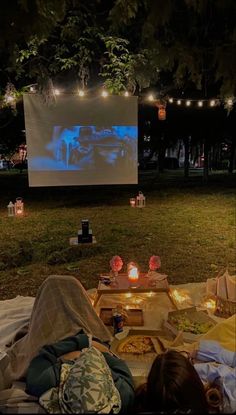 two people are watching a movie in the park at night with candles on the ground