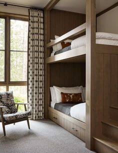 a bedroom with bunk beds and two chairs in front of a window that looks out onto the woods