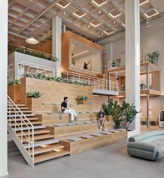 two people are sitting on the stairs in an open space with plants and couches