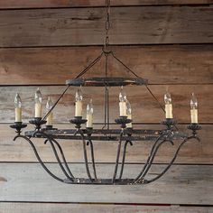 a chandelier with candles hanging from it's center, in front of a wooden wall