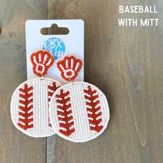 two red and white beaded baseball mitts on a wooden table next to a pair of earrings