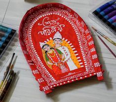 a red cloth covered with an image of two people on it, surrounded by crayons and markers