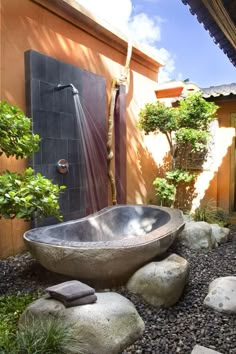 a bath tub sitting in the middle of a garden next to a tree and rocks