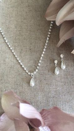 a necklace and earring set with pearls on a table next to pink flower petals