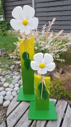 two green vases with white flowers in them sitting on a wooden table next to some rocks