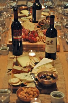 a wooden table topped with lots of wine bottles and plates filled with cheese, crackers and crackers