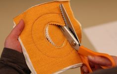 someone cutting fabric with scissors on top of an orange piece of cloth that has been cut in half