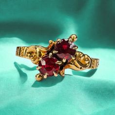 a gold ring with two red stones in it on a green cloth, close up