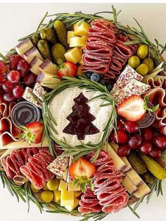 a platter filled with cheeses, meats and fruit arranged in the shape of a christmas tree