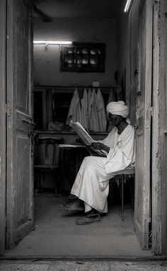 a man sitting on a chair reading a book in a room with wooden walls and doors