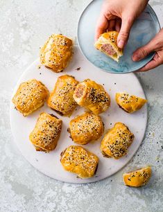 a plate full of ham and cheese sliders on a white platter with a hand reaching for one