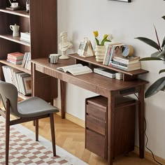 a wooden desk with books on it in front of a book shelf and planter