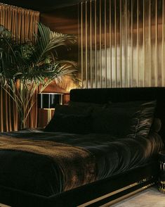 a bed with black sheets and pillows next to a plant in a room that has gold striped walls