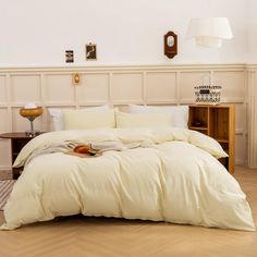 a bed with white sheets and pillows in a room next to a lamp on a table