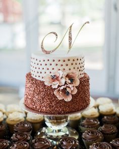 a three tiered cake with flowers on it and the number one on top is surrounded by cupcakes