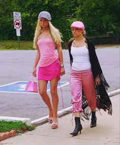 two women walking down the street with one holding a pink purse and another wearing a black hat