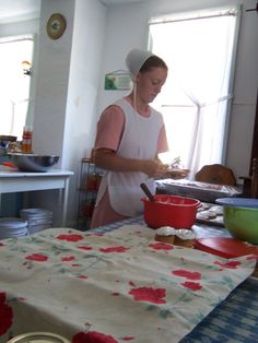 a woman is cooking in the kitchen with red bowls and utensils on the table