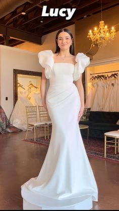 a woman standing in front of a white dress with ruffles on the shoulders