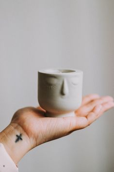 a person's hand holding a white cup with a face on it