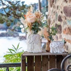 two vases filled with flowers sitting on top of a wooden table next to a stone wall