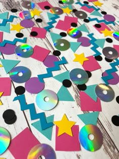 colorful paper cutouts and cd discs on a wooden table with white wood planks