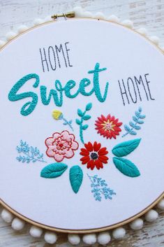 a hand embroidered hoop with the words home sweet home on it and flowers in front