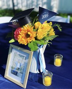 a vase with flowers and graduation caps on it is sitting on a table next to two shot glasses