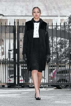 a woman is walking down the street in a black coat and dress with white collar