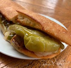 a sandwich with pickles and meat is on a white plate sitting on a wooden table