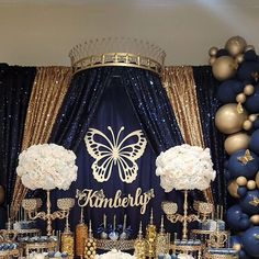 a blue and gold themed dessert table with white flowers, cake stands, and balloons