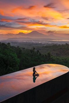 a person sitting on the edge of a swimming pool at sunset with mountains in the background